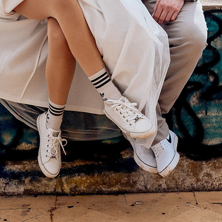 Detailaufnahme von Braut und Bräutigam mit weißen Sneakers, legerer Hochzeitslook vor Graffiti-Mauer