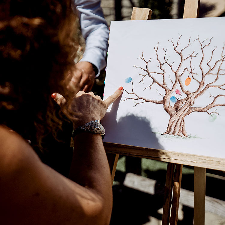 Hochzeitsgast setzt farbigen Fingerabdruck auf einen Hochzeitsbaum als Symbol für die freie Trauung