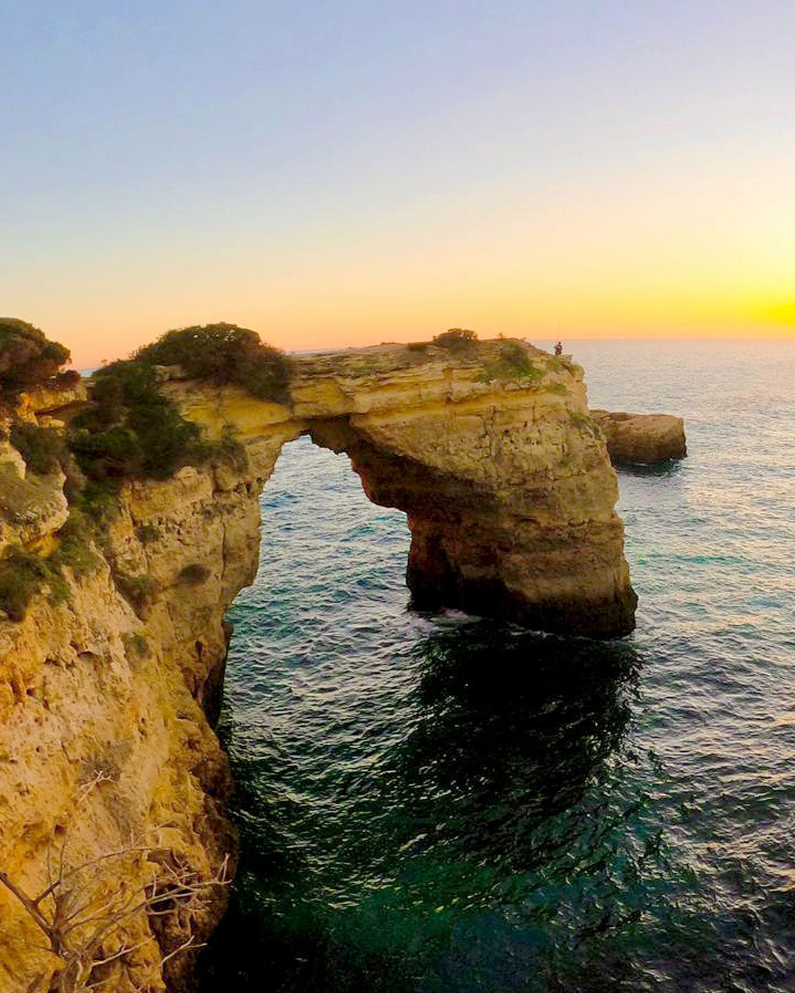 Sonnenuntergang über der Felsenküste und Bucht an der Algarve mit natürlichem Felsbogen