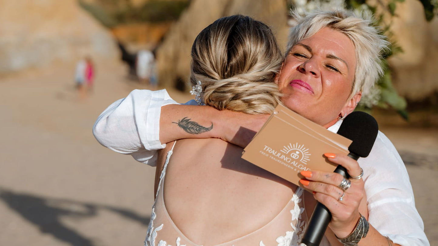 Braut und freie Rednerin umarmen sich herzlich nach der Trauung am Strand in Portugal, emotionaler Moment voller Dankbarkeit