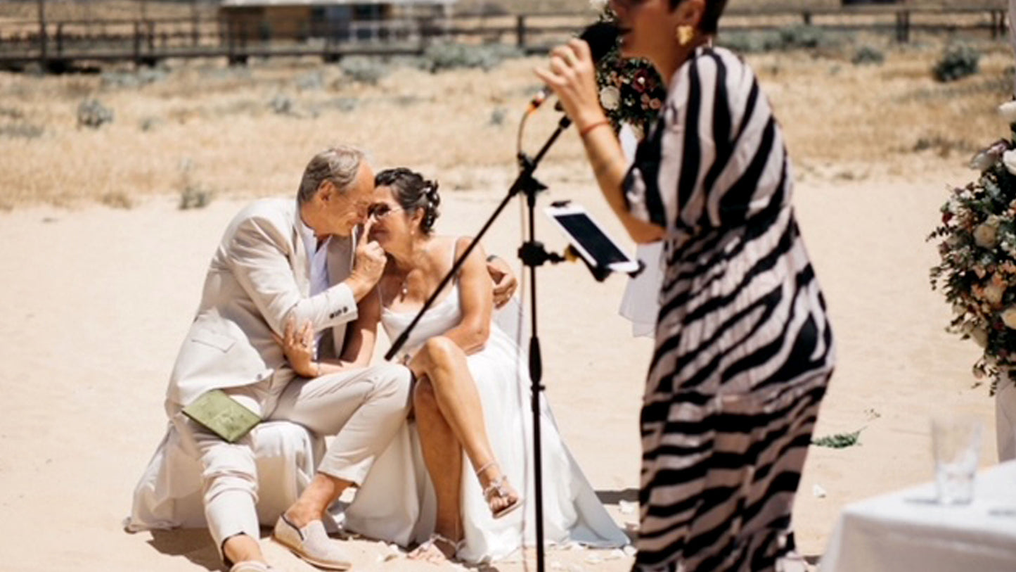 Goldene Hochzeit am Strand in Portugal, Brautpaar sitzt innig zusammen während die freie Rednerin die Zeremonie hält