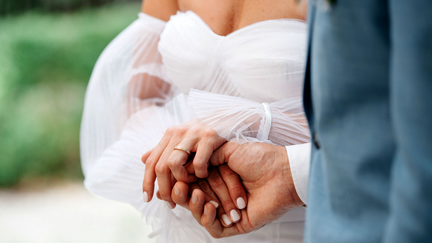 Braut und Bräutigam halten sich bei der freien Trauung die Hände, goldener Ehering sichtbar