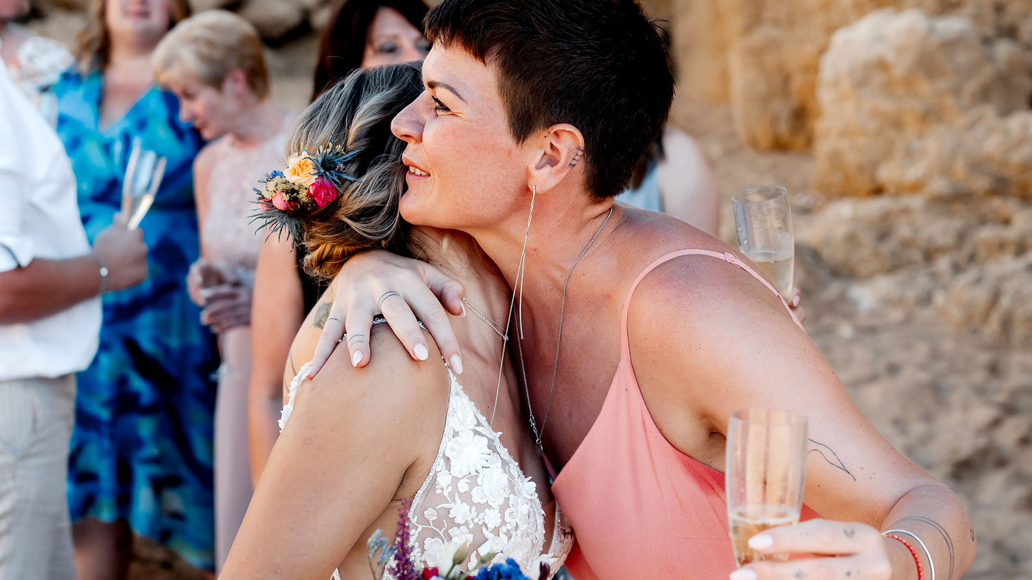 Braut und freie Rednerin umarmen sich herzlich bei der Hochzeit am Strand in Portugal, Feier mit Gästen