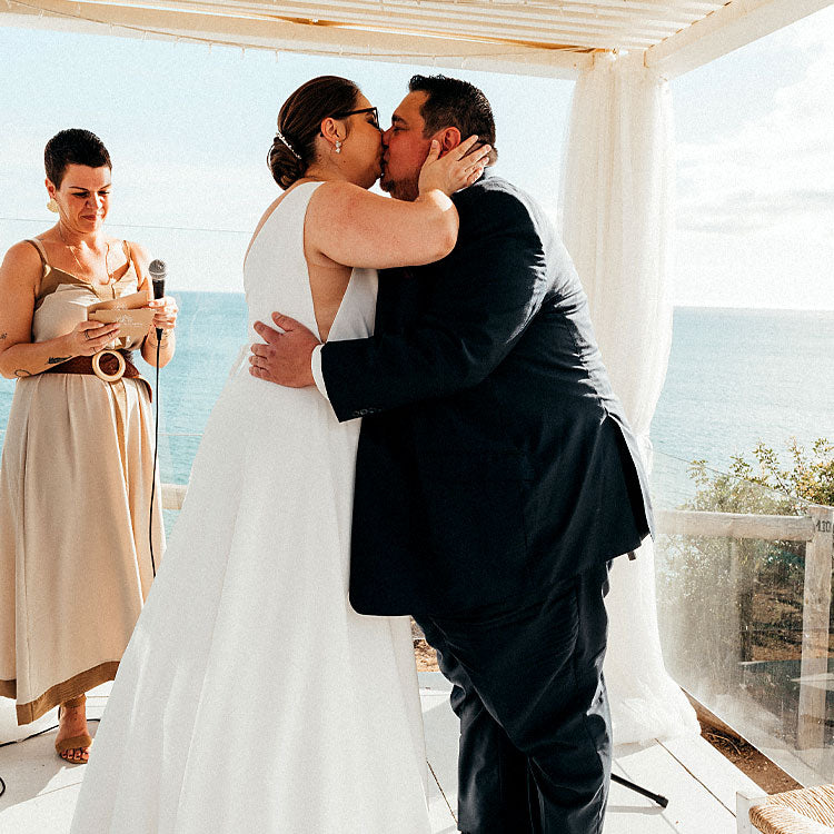 Brautpaar küsst sich bei der freien Trauung am Meer in Portugal, Traurednerin spricht die persönliche Zeremonie