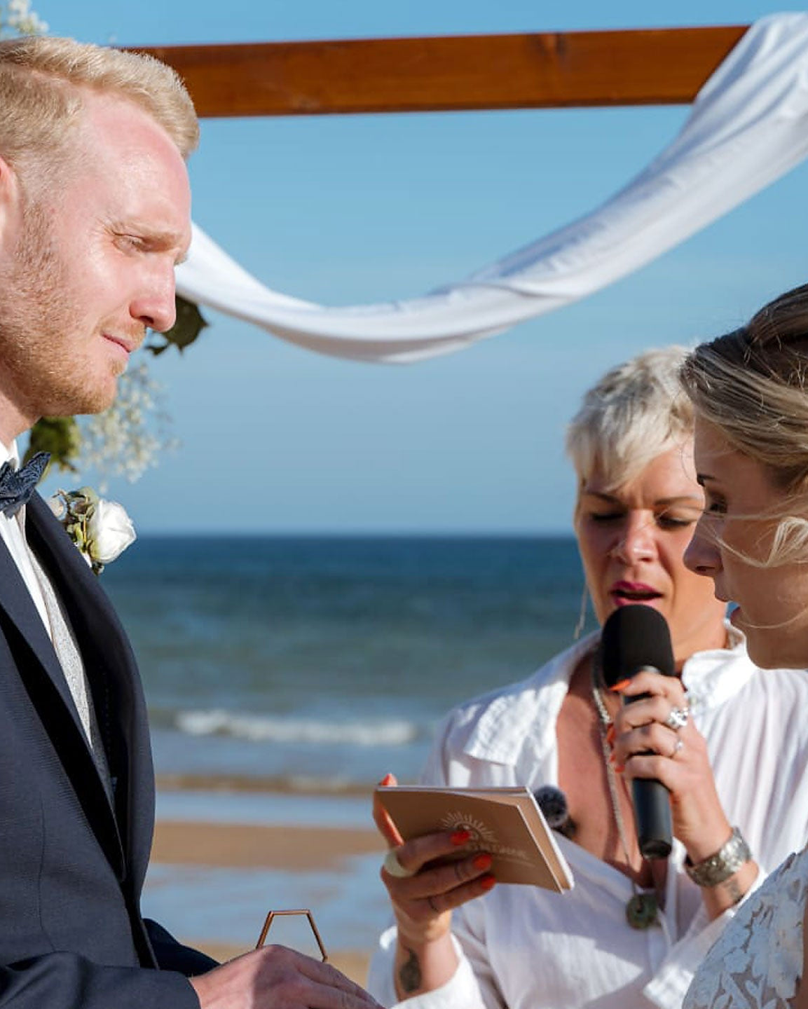 Brautpaar bei freier Trauung am Strand der Algarve mit Traurednerin vor Blumenbogen