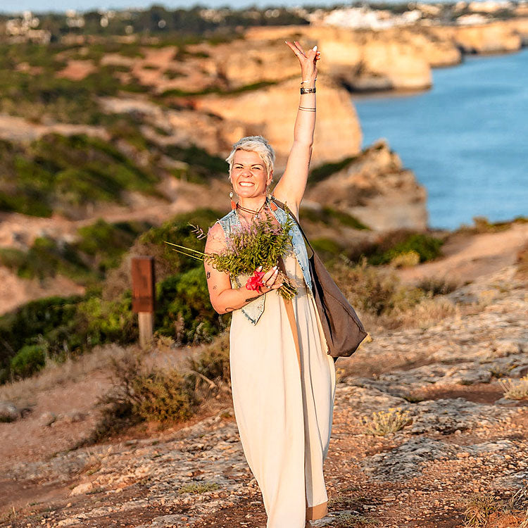 Susy Stocky – freie Traurednerin in der Algarve, strahlend mit Blumenstrauß an der Felsküste Portugals