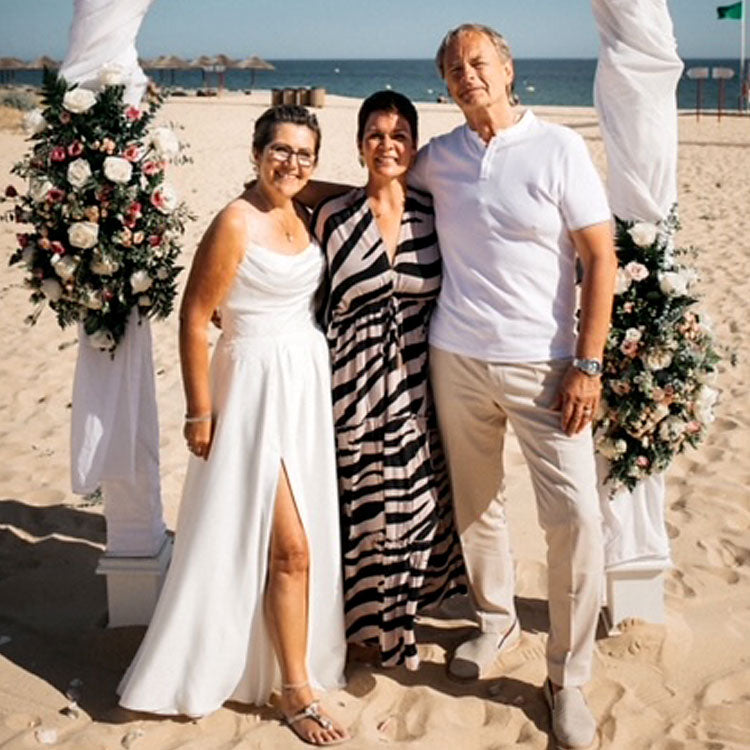 Brautpaar mit freier Rednerin nach der Trauung am Strand in Portugal, festlich geschmückter Traubogen mit Blumen