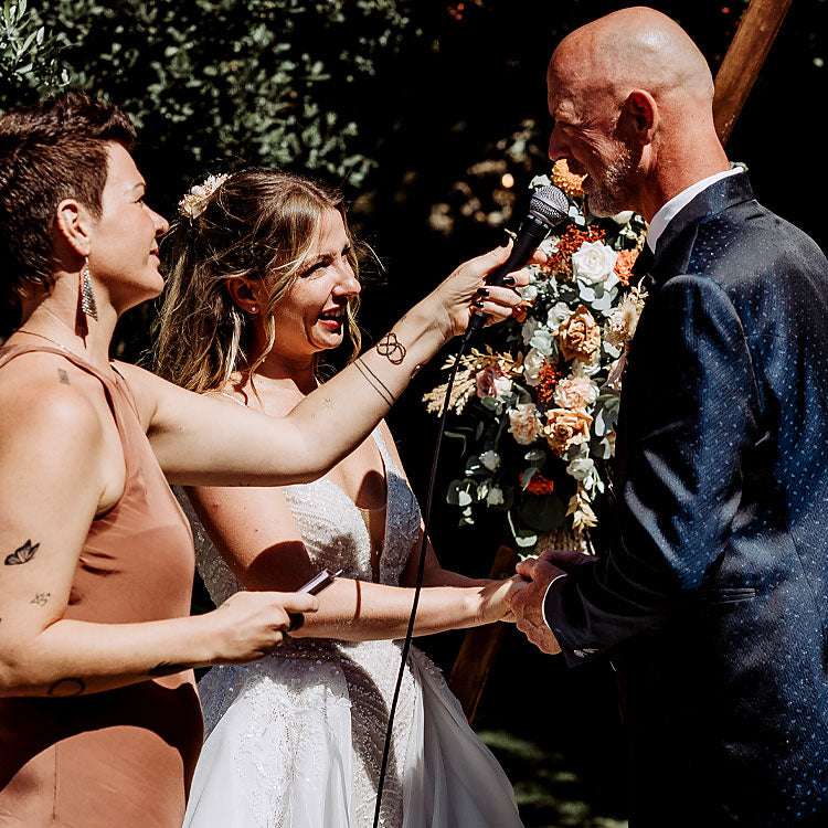 Brautpaar gibt sich das Eheversprechen bei einer freien Trauung, Traurednerin hält das Mikrofon während der Zeremonie